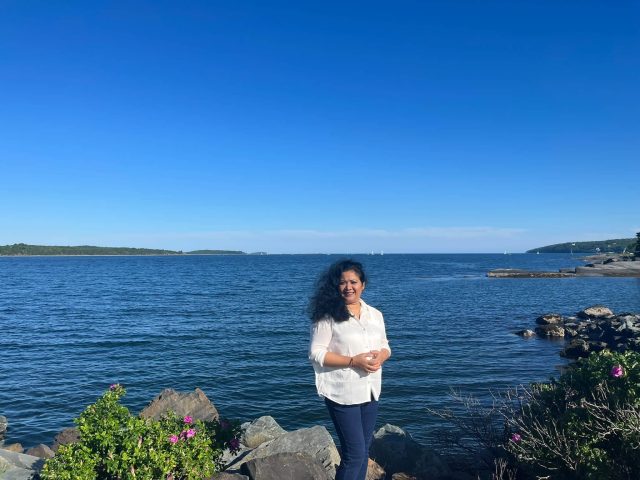 Editor Nasrin Nahar Jeneva stands confidently with a smiling face beside the Atlantic Ocean, exemplifying leadership and positivity.