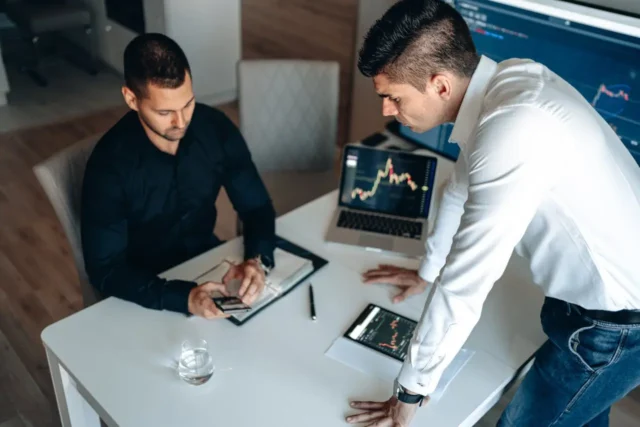 Two business professionals analyzing financial data on multiple devices in an office setting, representing the impact of rising interest rates on global markets.