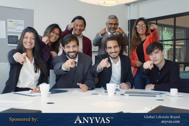 A team of professionals confidently pointing toward the camera, symbolizing leadership, people management, and teamwork, in a modern office environment. Sponsored by Anyvas, Global Lifestyle Brand.