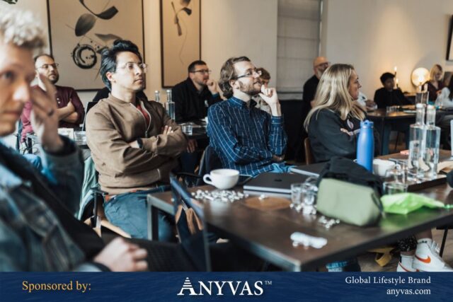 Group of diverse professionals attentively participating in a workshop or seminar, seated around tables with laptops, coffee cups, and note-taking materials.