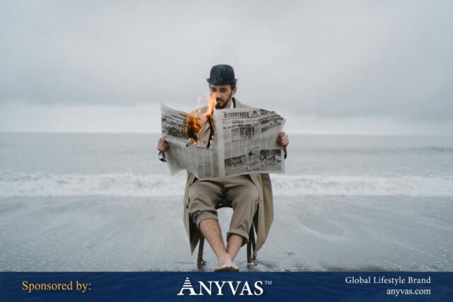 A man sits barefoot on a chair at the shoreline, calmly reading a burning newspaper, with ocean waves behind him and a dramatic sky above. Sponsored by ANYVAS.